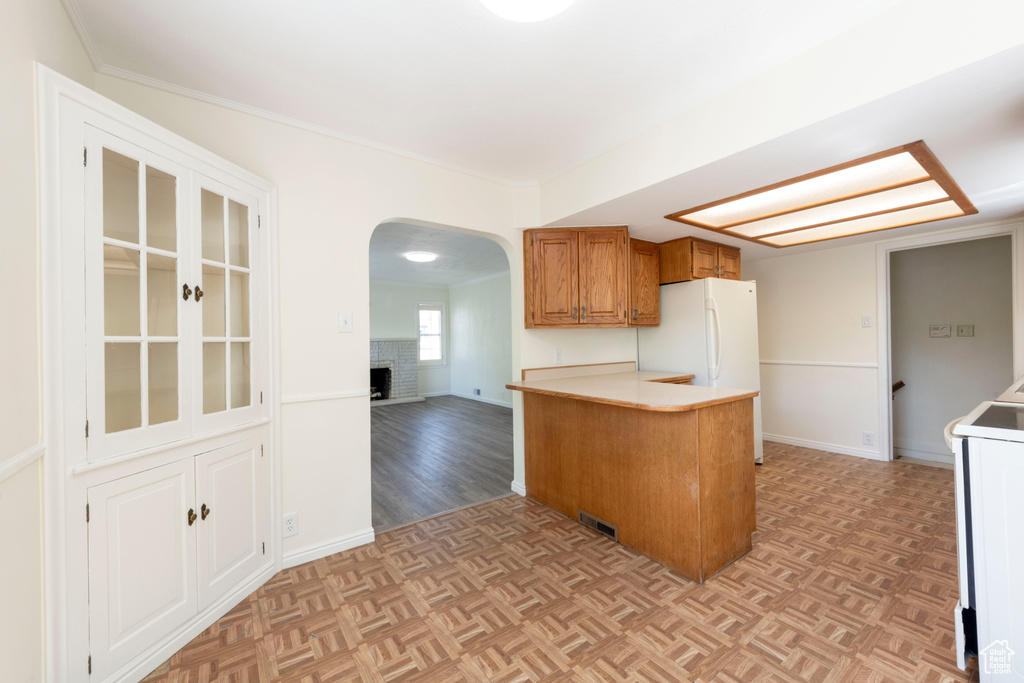 Kitchen featuring arched walkways, freestanding refrigerator, brown cabinets, a peninsula, and range