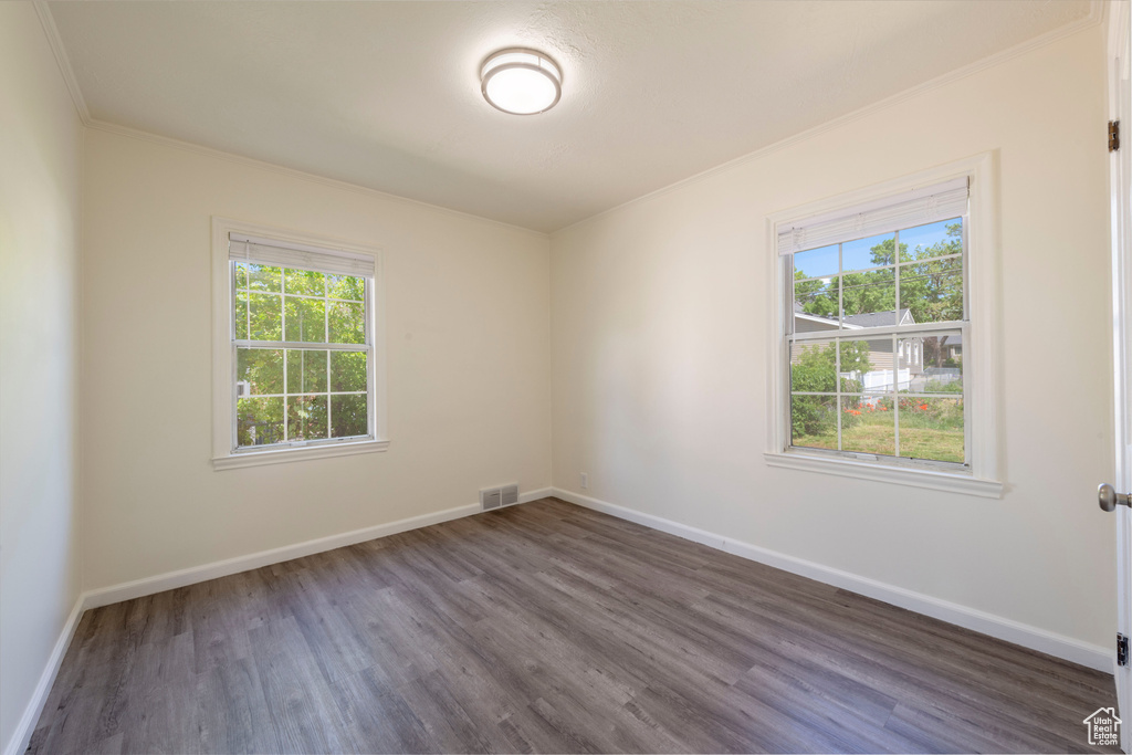 Spare room featuring dark wood-style flooring, baseboards, and crown molding