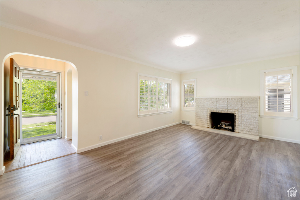 Unfurnished living room with wood finished floors, crown molding, healthy amount of natural light, arched walkways, and a fireplace