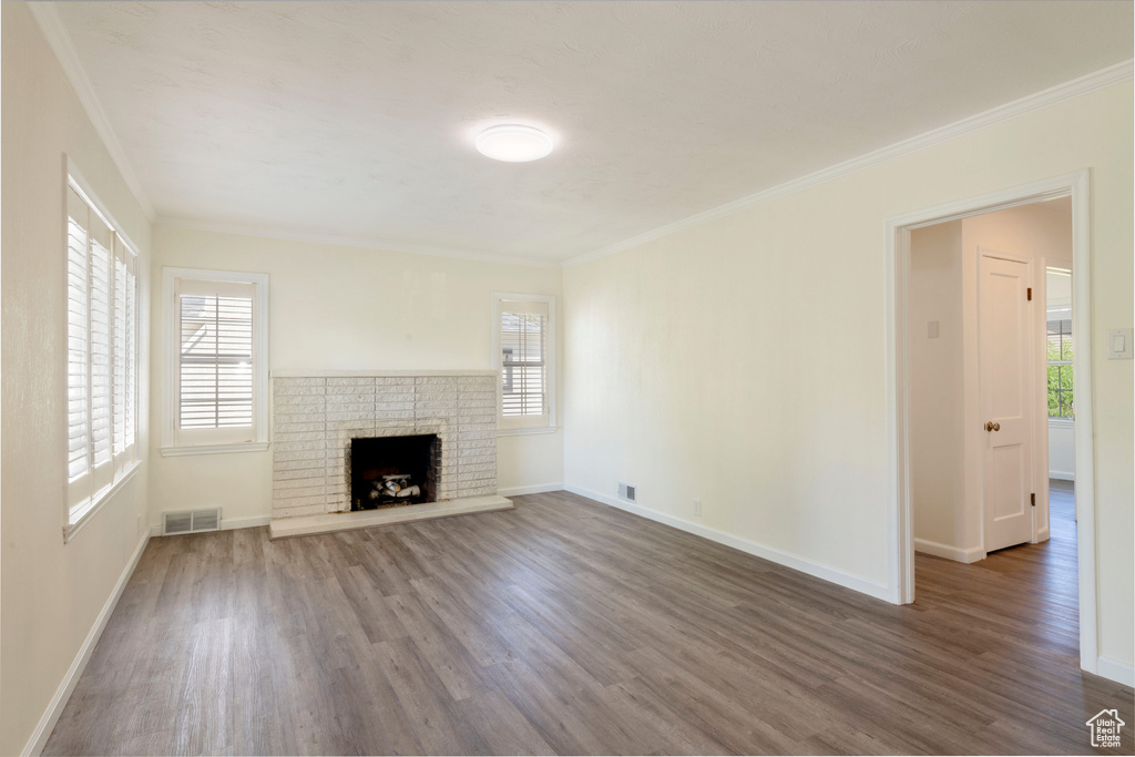 Unfurnished living room with wood finished floors, plenty of natural light, crown molding, and baseboards