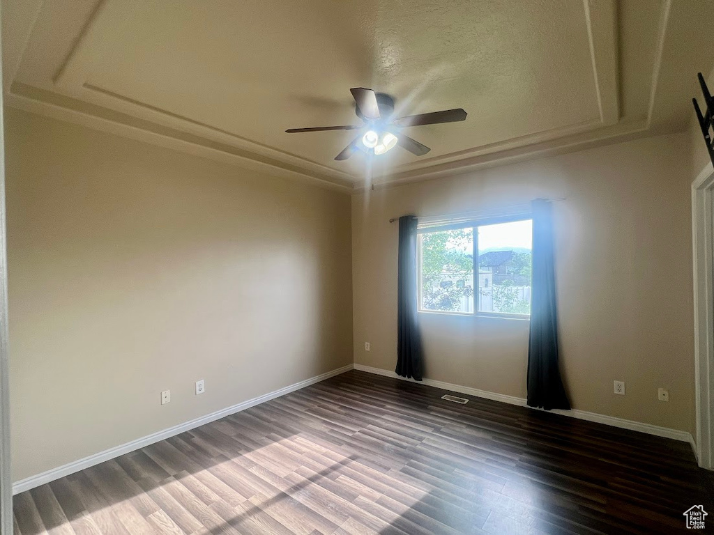 Empty room featuring wood finished floors, a ceiling fan, a tray ceiling, and baseboards