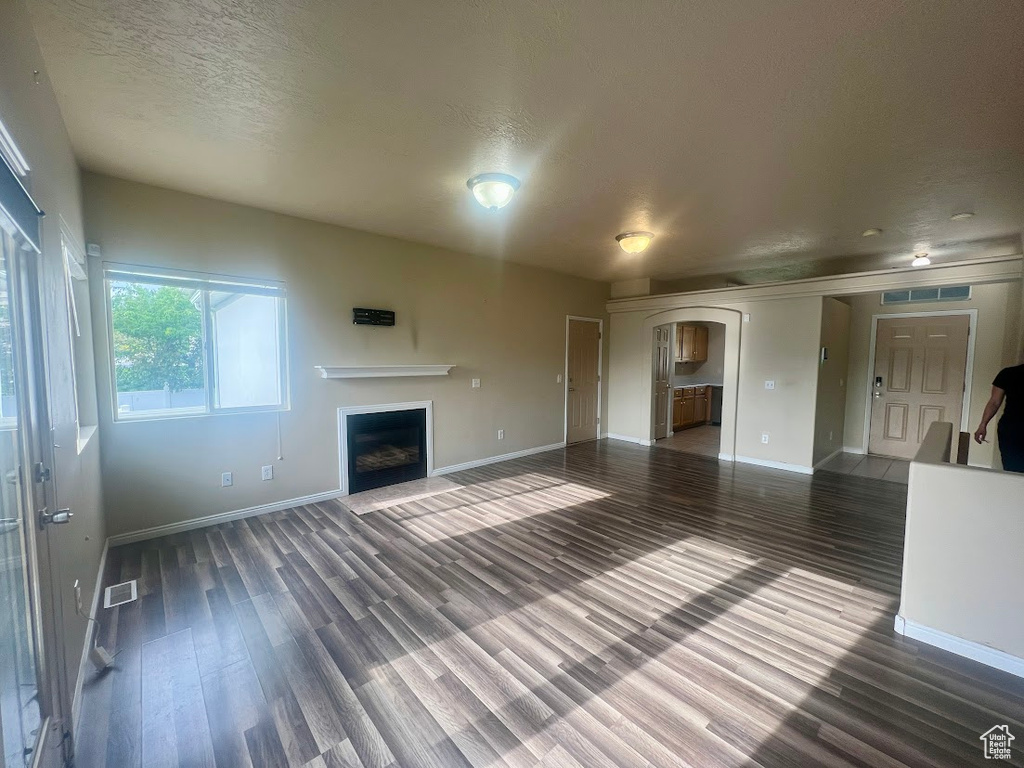 Unfurnished living room featuring baseboards, wood finished floors, a fireplace, arched walkways, and a textured ceiling
