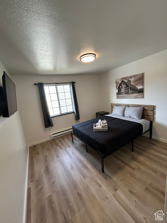 Bedroom with light wood-type flooring, a baseboard radiator, a textured ceiling, and baseboards