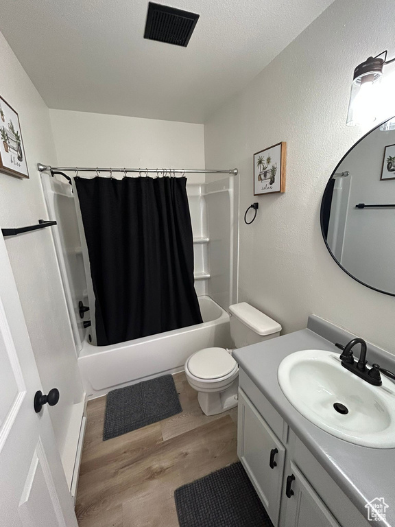 Bathroom with wood finished floors, vanity, shower / bath combination with curtain, toilet, and a textured ceiling
