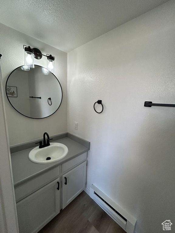 Bathroom featuring baseboard heating, wood finished floors, vanity, and a textured ceiling