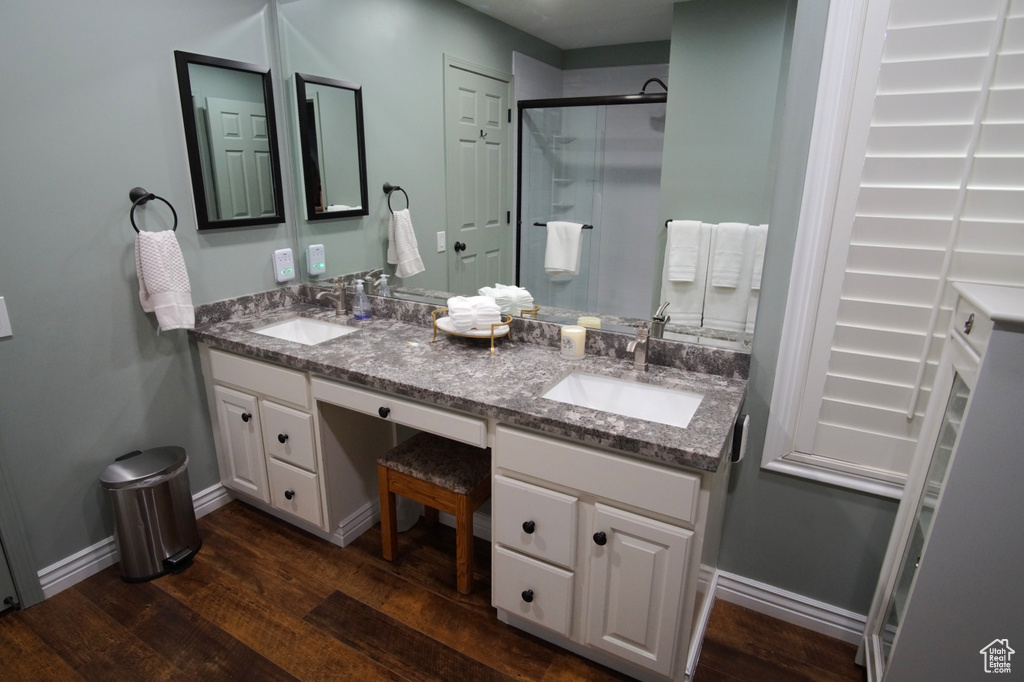 Full bathroom with a stall shower, double vanity, wood finished floors, and baseboards