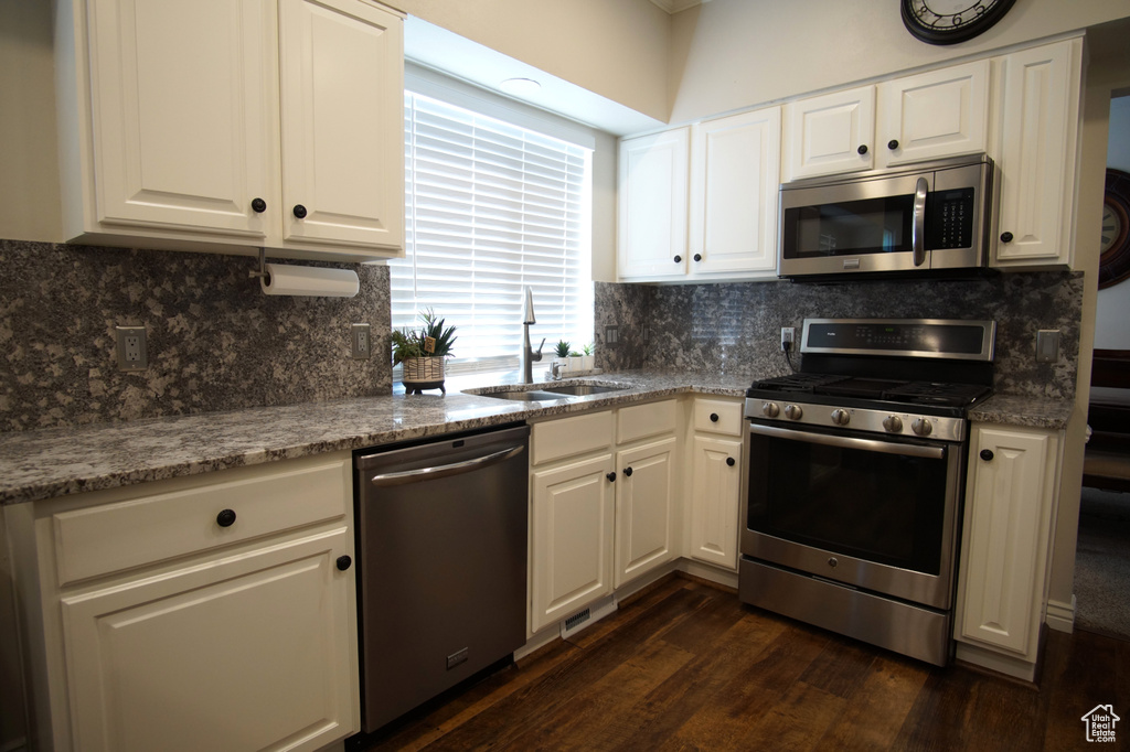Kitchen with appliances with stainless steel finishes, a sink, dark wood finished floors, and white cabinetry