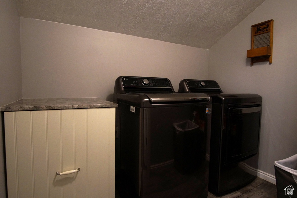 Laundry area with a textured ceiling, washing machine and dryer, wood finished floors, and baseboards