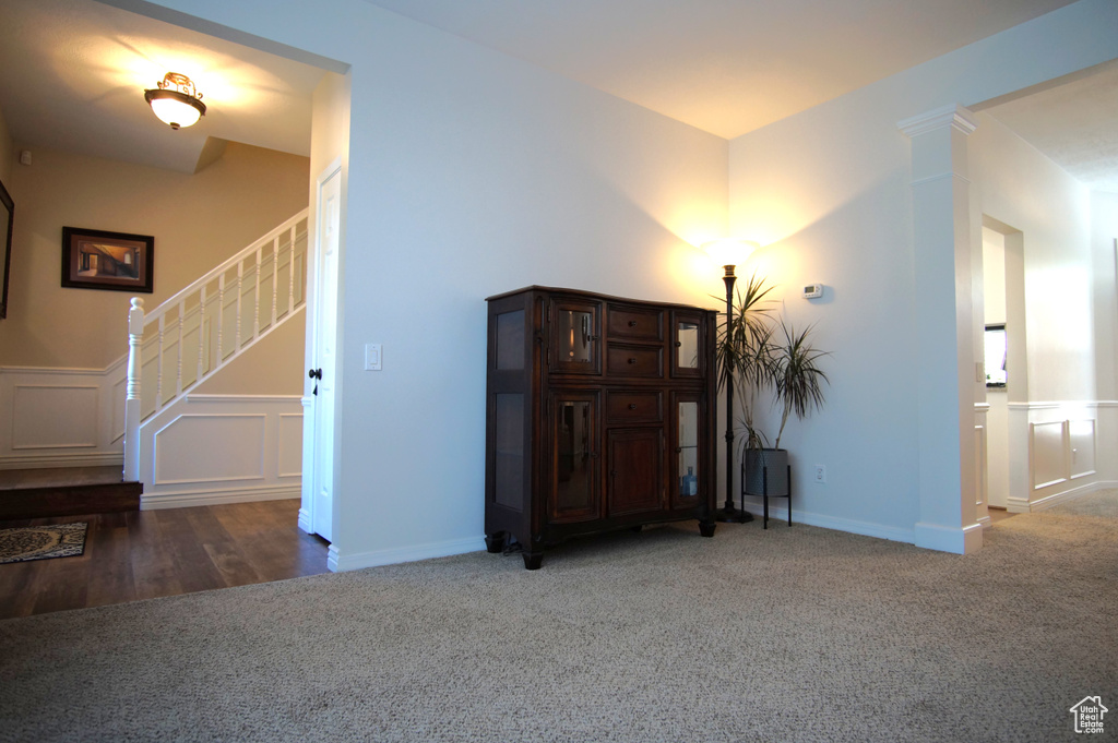Carpeted living room featuring stairs, a decorative wall, and wainscoting