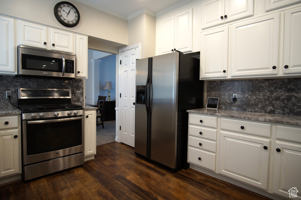 Kitchen with stainless steel appliances, ornamental molding, white cabinets, tasteful backsplash, and dark wood-style flooring