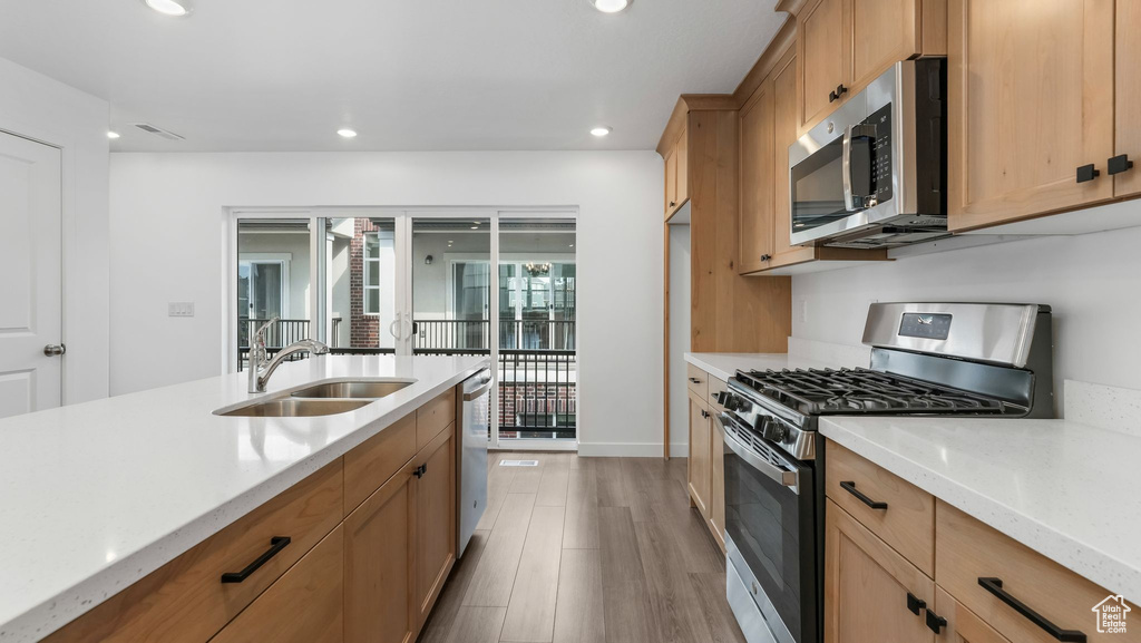Kitchen featuring appliances with stainless steel finishes, recessed lighting, wood finished floors, and light stone counters
