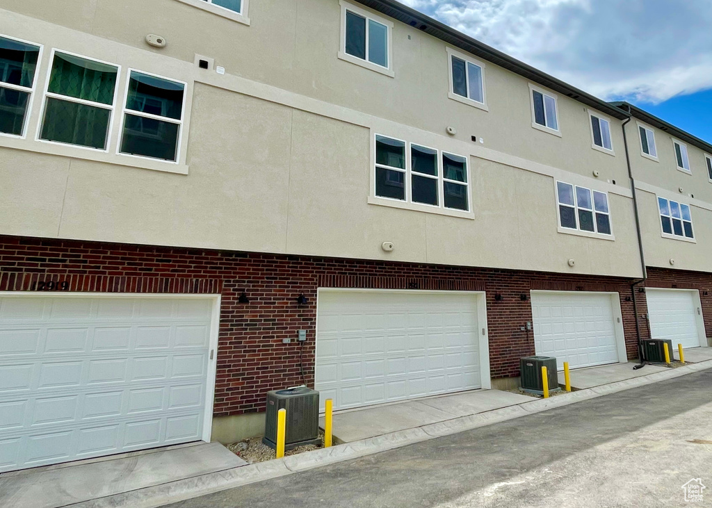 Back of property featuring central AC unit, stucco siding, brick siding, and a garage
