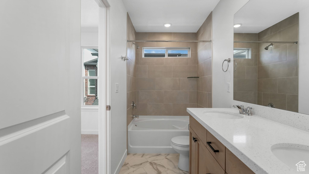 Bathroom featuring washtub / shower combination, double vanity, and marble look tile flooring