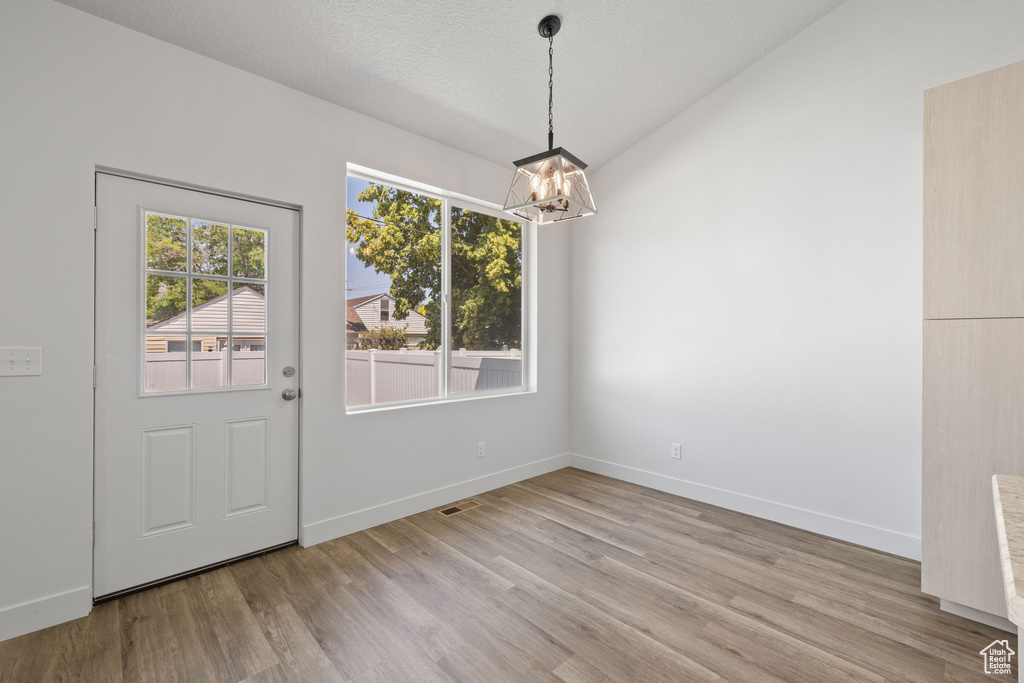 Unfurnished dining area featuring a chandelier, light wood-type flooring, and lofted ceiling