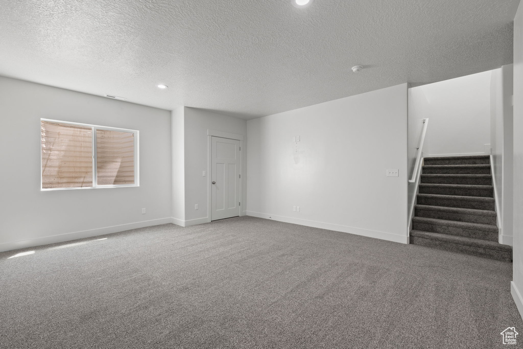 Unfurnished living room with a textured ceiling, carpet floors, stairs, and recessed lighting