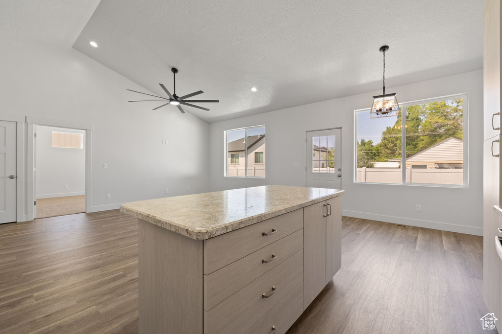 Kitchen with wood finished floors, a ceiling fan, a kitchen island, pendant lighting, and a chandelier