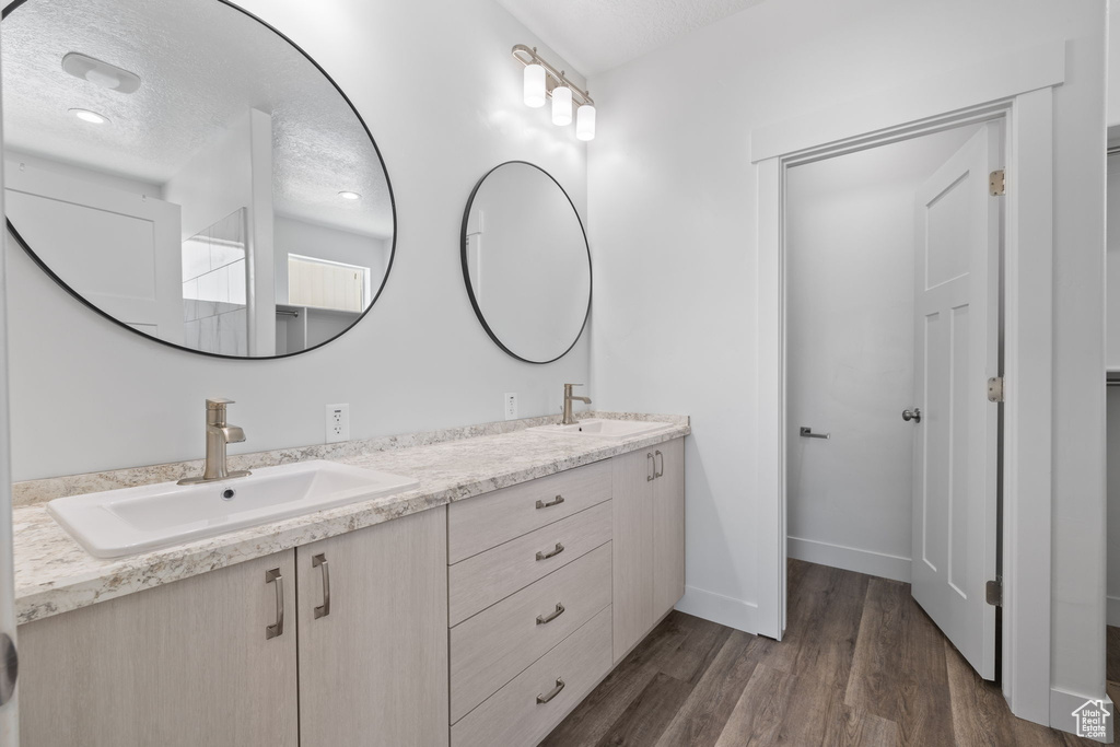 Bathroom with double vanity, wood finished floors, and a textured ceiling