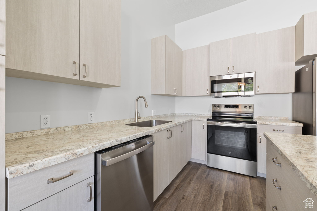 Kitchen with appliances with stainless steel finishes, dark wood-type flooring, light brown cabinets, and light stone counters