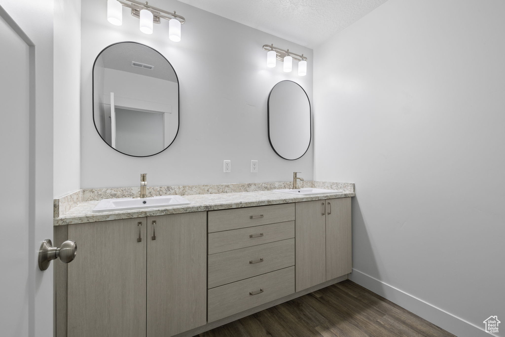 Bathroom with double vanity, wood finished floors, and a textured ceiling