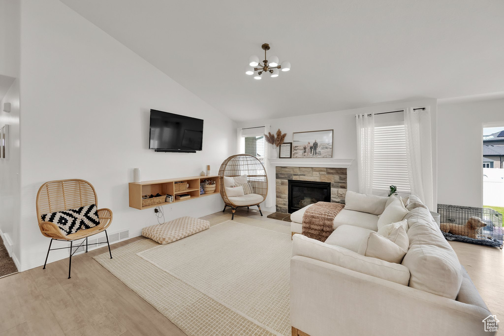 Living room featuring a stone fireplace, wood finished floors, a chandelier, baseboards, and high vaulted ceiling