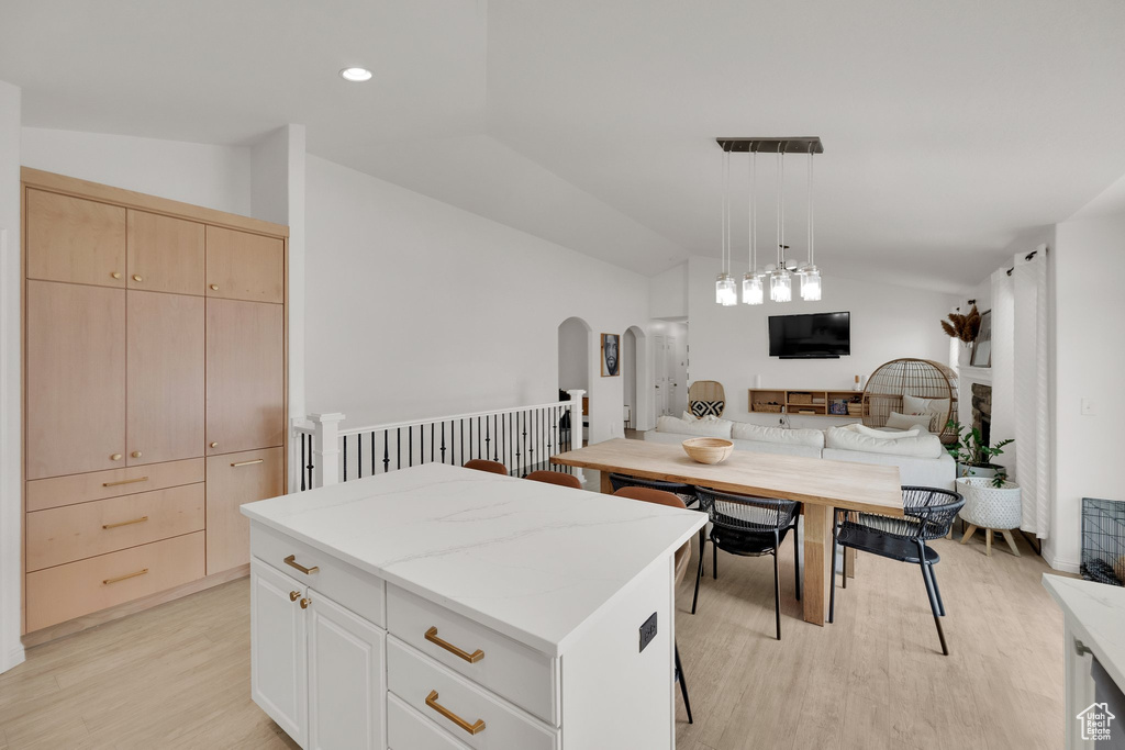Kitchen featuring lofted ceiling, open floor plan, light wood-style floors, arched walkways, and a kitchen island