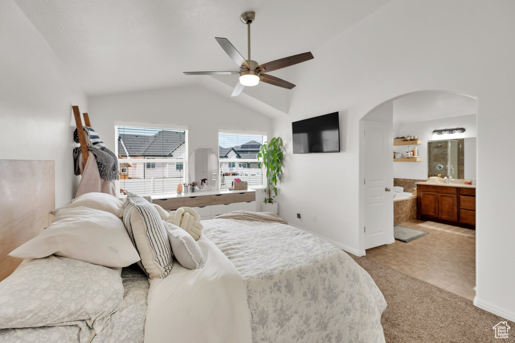 Bedroom featuring arched walkways, lofted ceiling, baseboards, ensuite bathroom, and light colored carpet