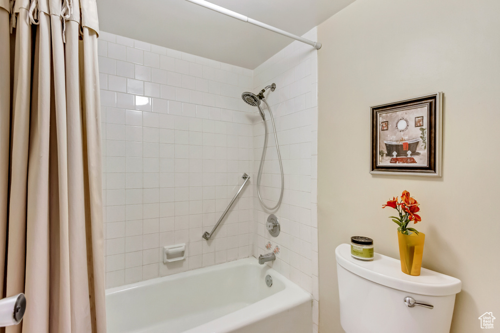 Bathroom featuring toilet and shower / bath combination with curtain