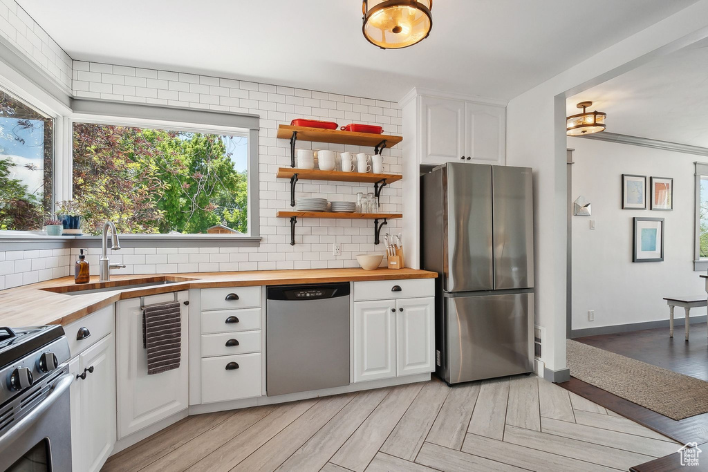 Kitchen with appliances with stainless steel finishes, butcher block countertops, a sink, and decorative backsplash