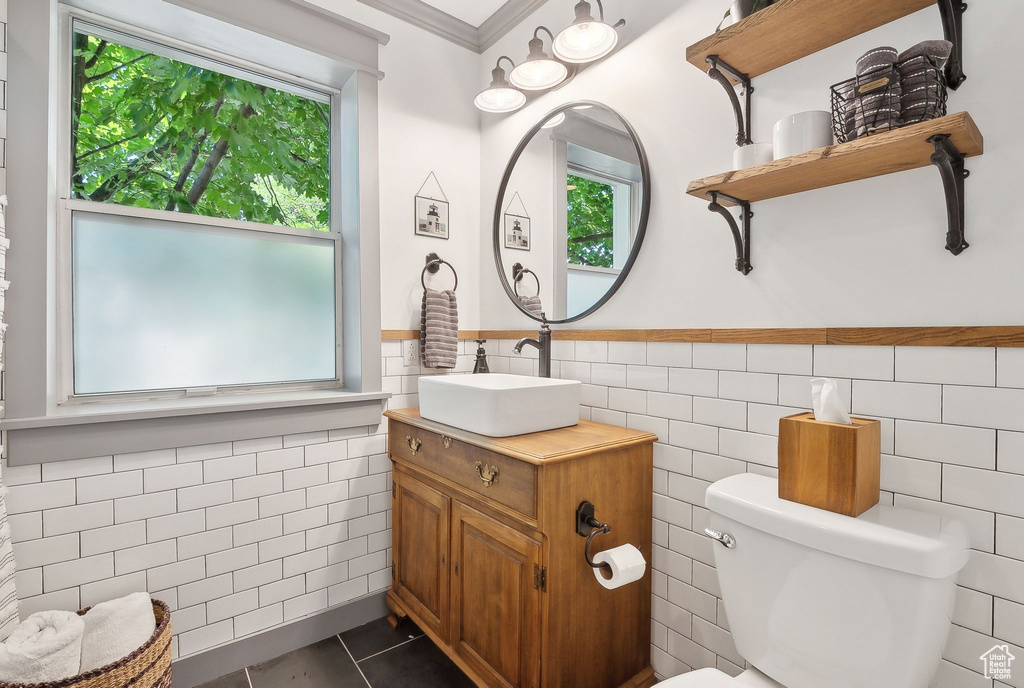 Bathroom featuring tile walls, vanity, toilet, tile patterned floors, and a wainscoted wall