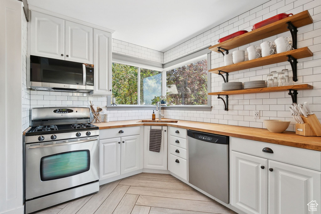 Kitchen with stainless steel appliances, wooden counters, a sink, and decorative backsplash