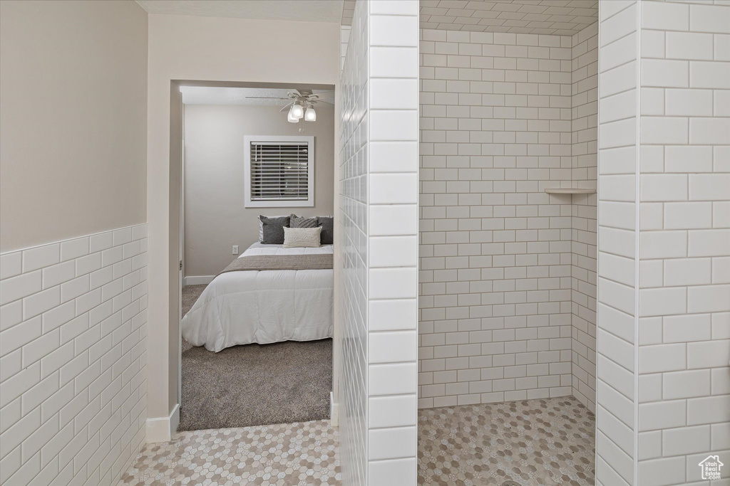 Full bath with tiled shower, ensuite bathroom, a ceiling fan, and tile walls