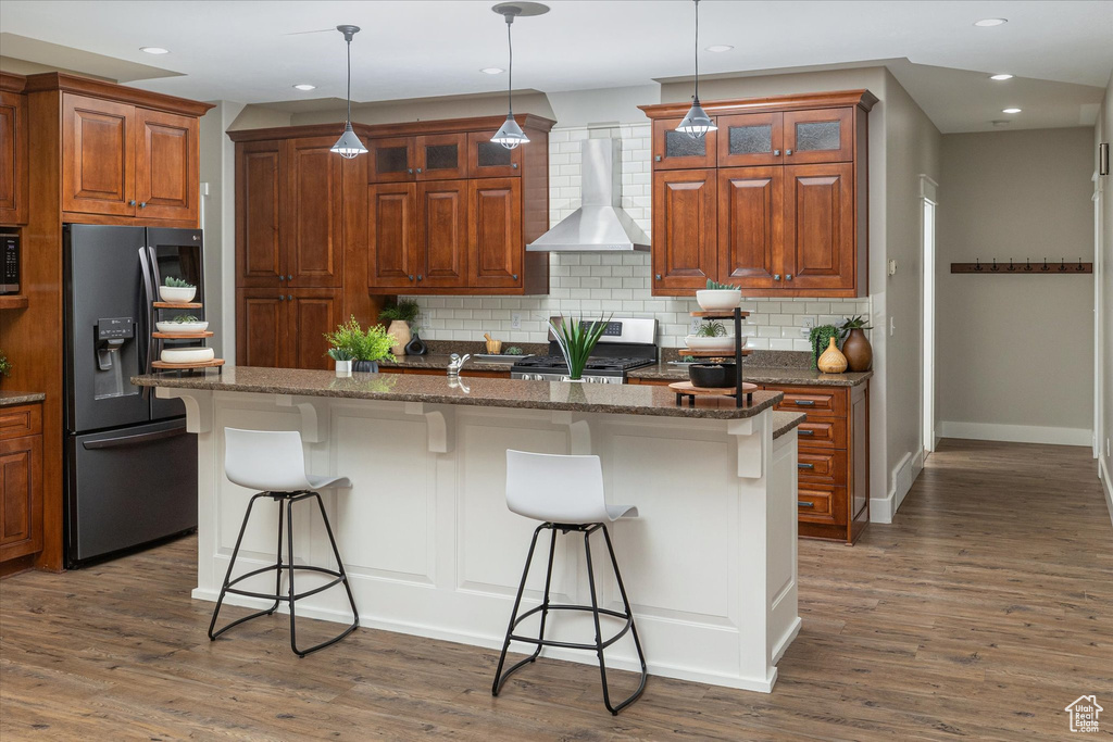 Kitchen with appliances with stainless steel finishes, wall chimney range hood, a kitchen bar, decorative backsplash, and wood finished floors