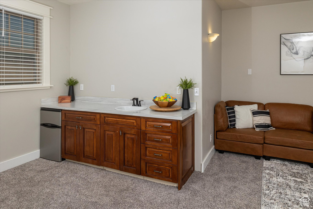 Bar area featuring freestanding refrigerator, light carpet, a sink, and baseboards