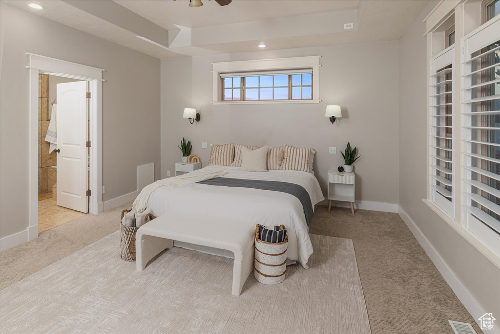 Carpeted bedroom with a tray ceiling, ensuite bath, baseboards, and recessed lighting