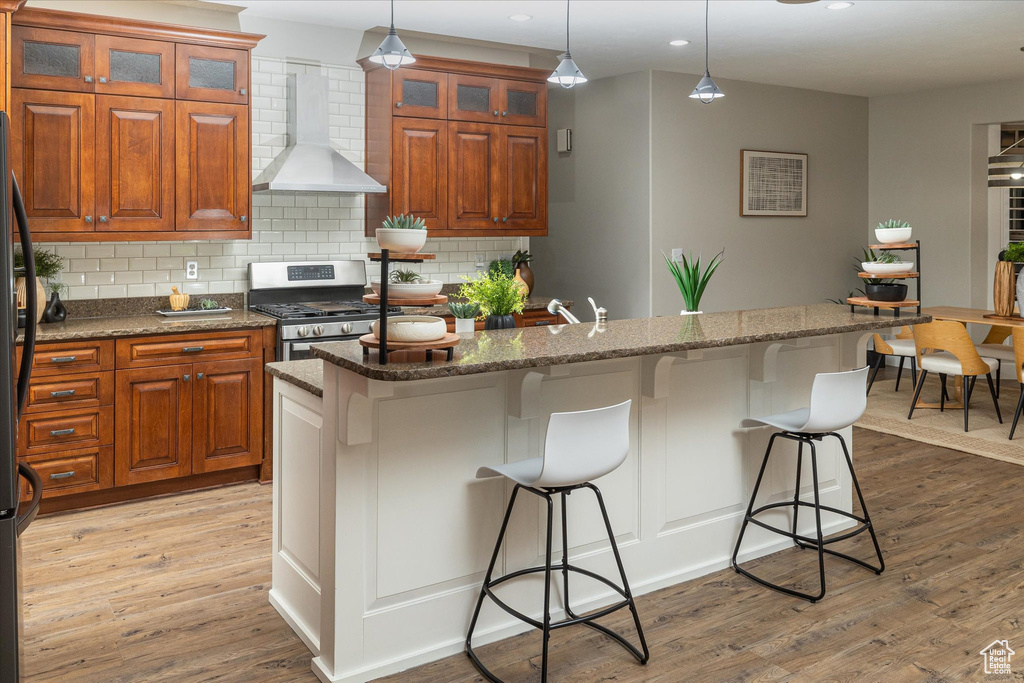 Kitchen featuring wall chimney range hood, stainless steel gas range, light wood-style flooring, recessed lighting, and tasteful backsplash
