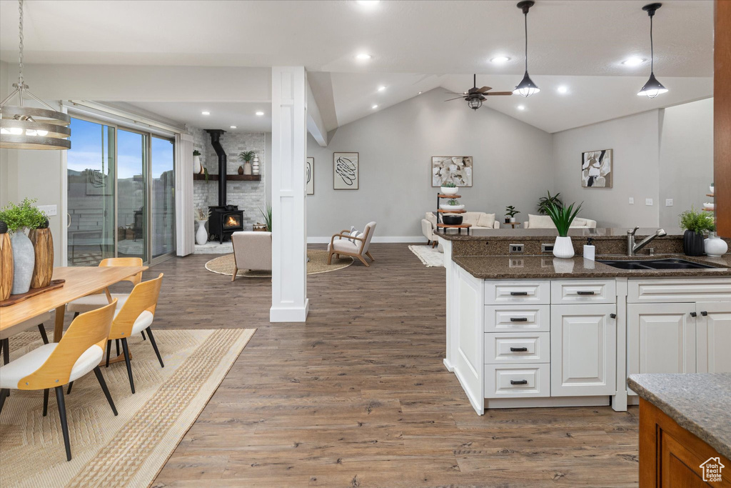 Kitchen with a sink, a wood stove, white cabinetry, vaulted ceiling, and wood finished floors
