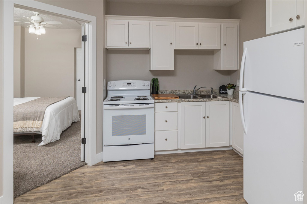 Kitchen with white appliances, a sink, wood finished floors, and white cabinets