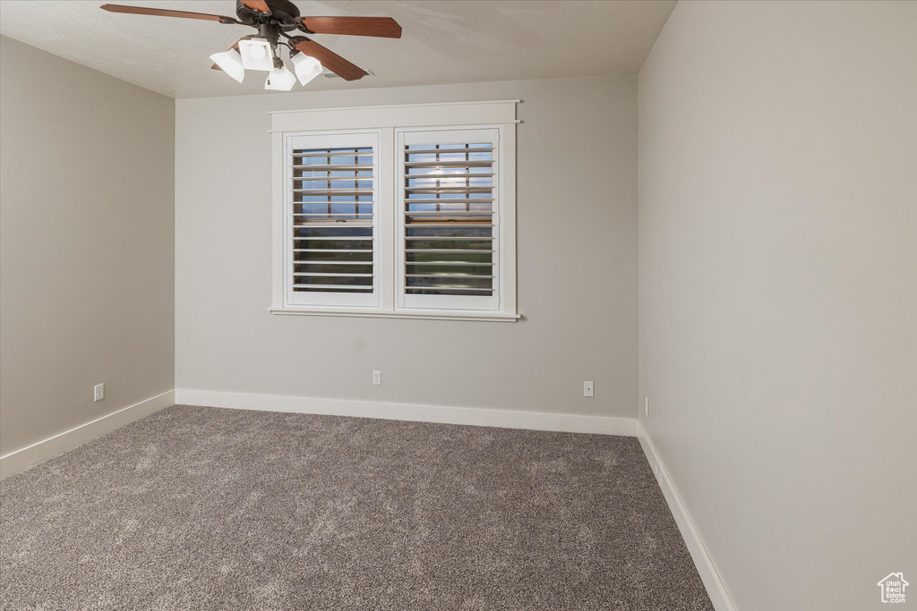 Carpeted empty room featuring ceiling fan and baseboards