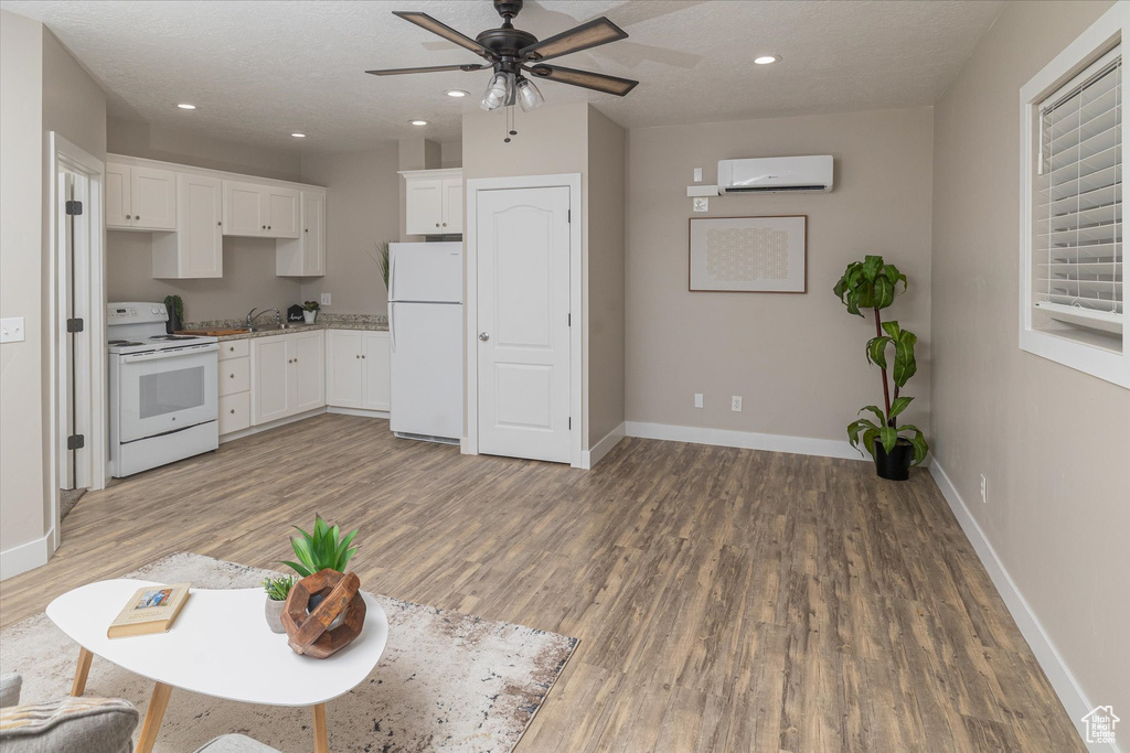 Kitchen featuring white appliances, an AC wall unit, light wood finished floors, a ceiling fan, and baseboards