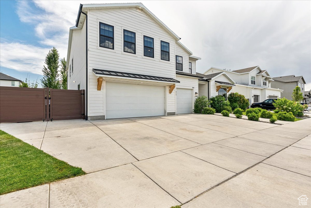 View of front of property featuring a standing seam roof, a gate, an attached garage, metal roof, and concrete driveway
