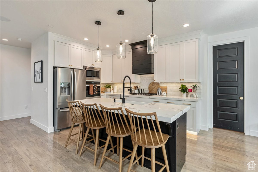 Kitchen featuring appliances with stainless steel finishes, baseboards, light countertops, a breakfast bar area, and decorative backsplash