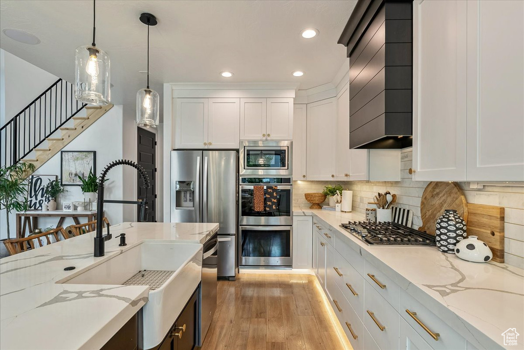 Kitchen with stainless steel appliances, a sink, recessed lighting, wall chimney exhaust hood, and light wood-style floors