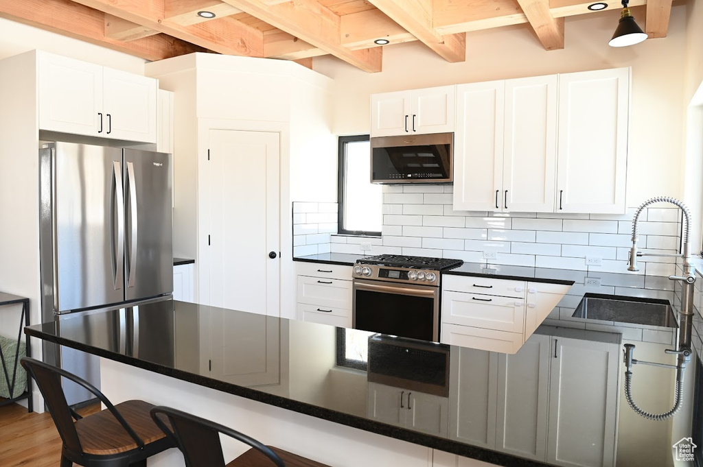 Kitchen with appliances with stainless steel finishes, beamed ceiling, dark countertops, a kitchen breakfast bar, and decorative backsplash
