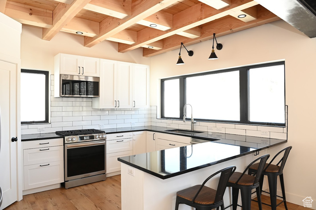 Kitchen featuring appliances with stainless steel finishes, a sink, dark countertops, backsplash, and wood ceiling with exposed beams