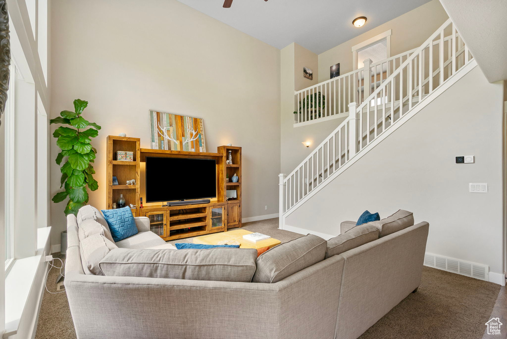 Living area with carpet flooring, stairs, baseboards, a ceiling fan, and a towering ceiling
