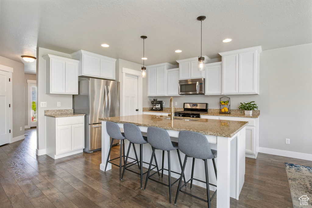 Kitchen featuring appliances with stainless steel finishes, baseboards, dark wood finished floors, an island with sink, and a kitchen bar