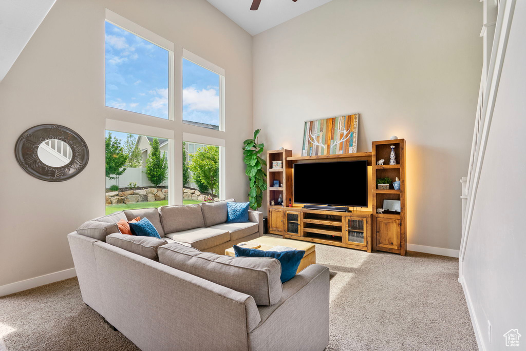 Living room featuring carpet flooring, baseboards, a ceiling fan, and a towering ceiling