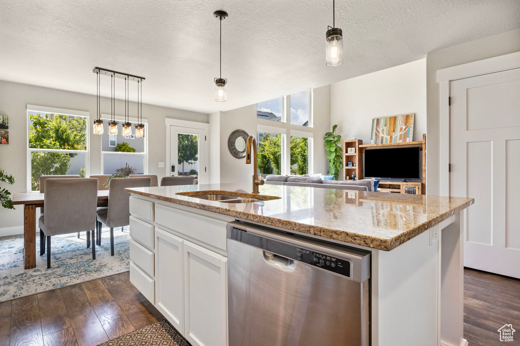 Kitchen featuring stainless steel dishwasher, a sink, plenty of natural light, an island with sink, and a textured ceiling