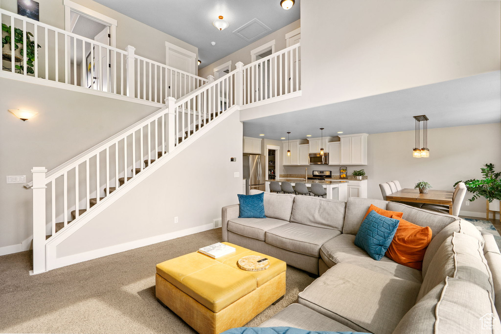 Carpeted living room with a towering ceiling, stairway, and baseboards