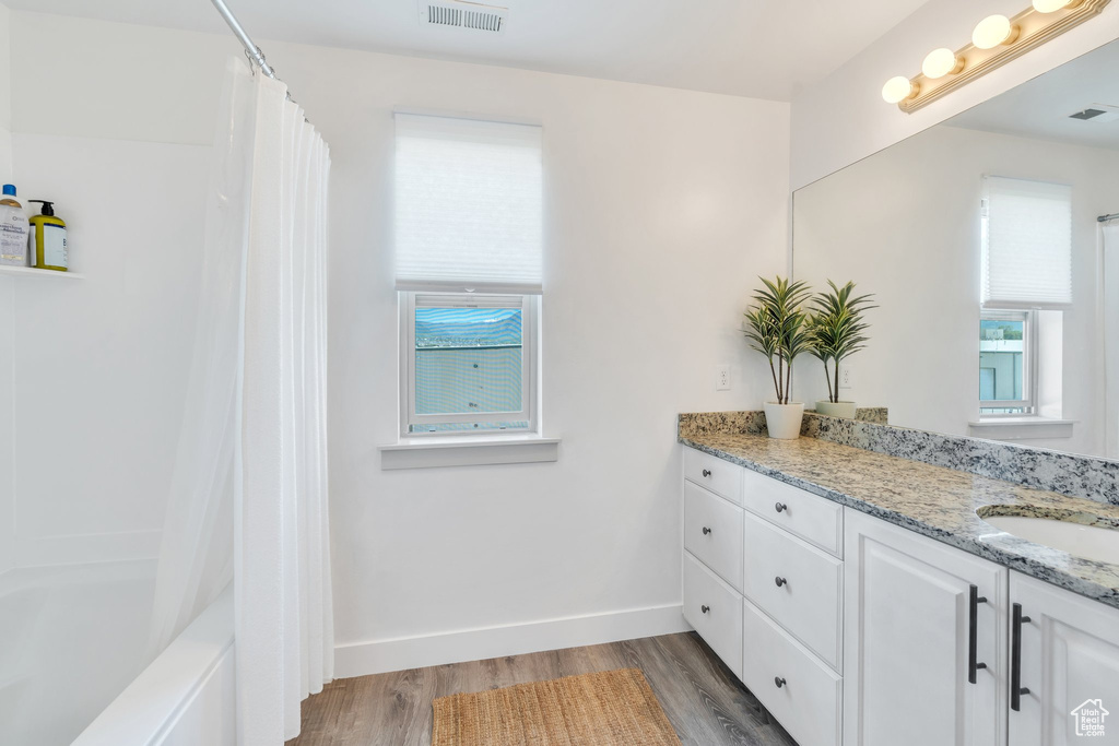 Bathroom featuring vanity, wood finished floors, shower / bath combination with curtain, and baseboards